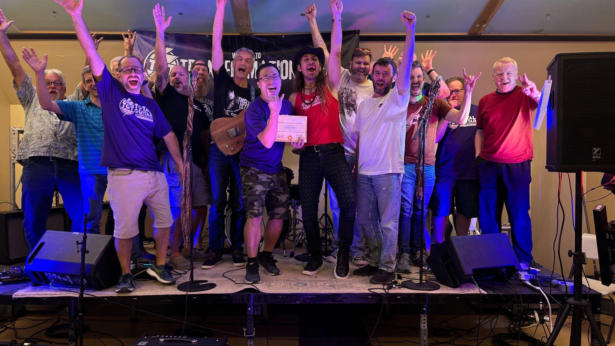 A diverse group of people celebrating on stage with raised arms and instruments