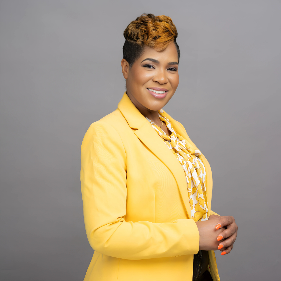Smiling woman in a bright yellow suit against a gray background.