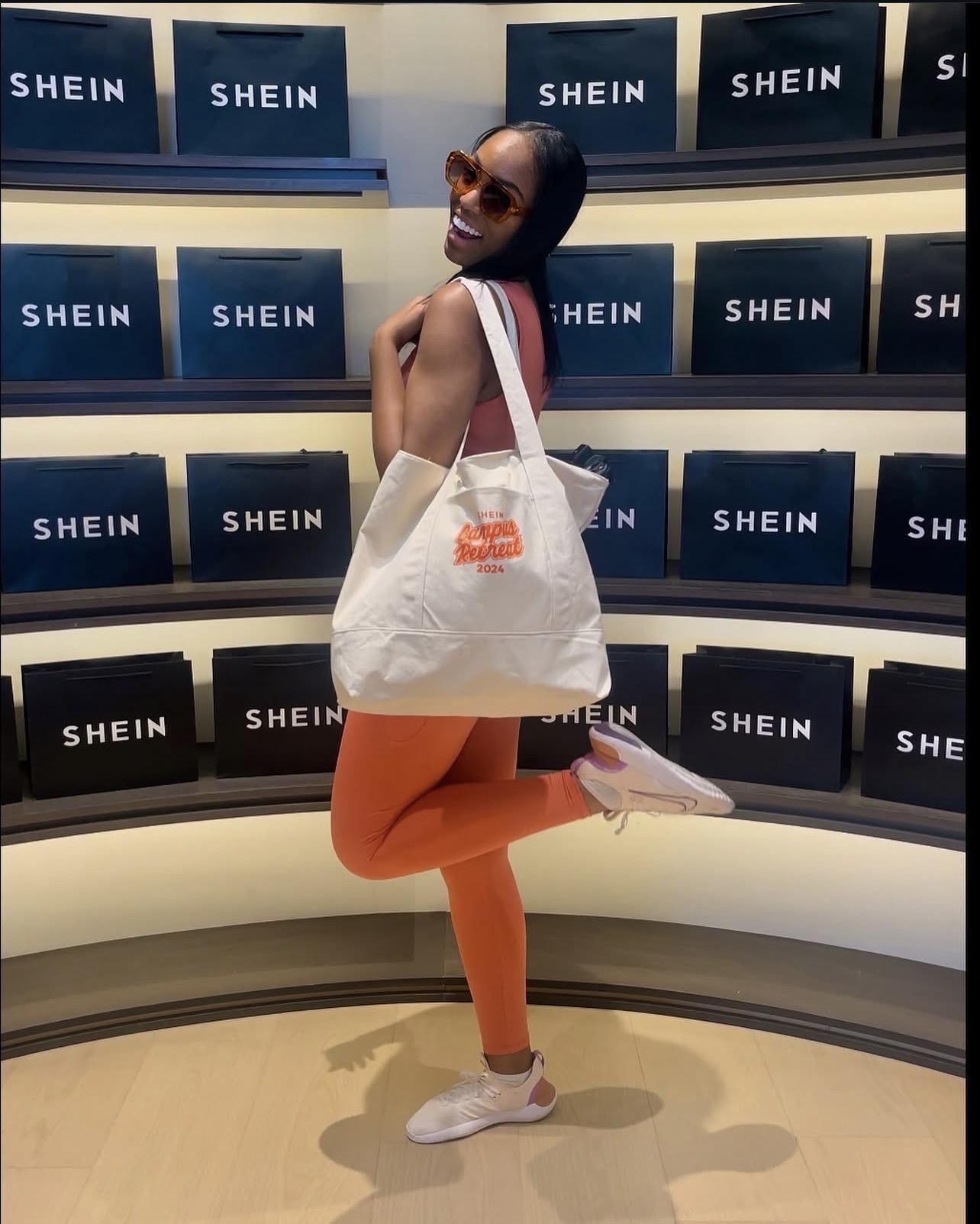A woman poses in a store, holding a tote bag and wearing stylish sunglasses.