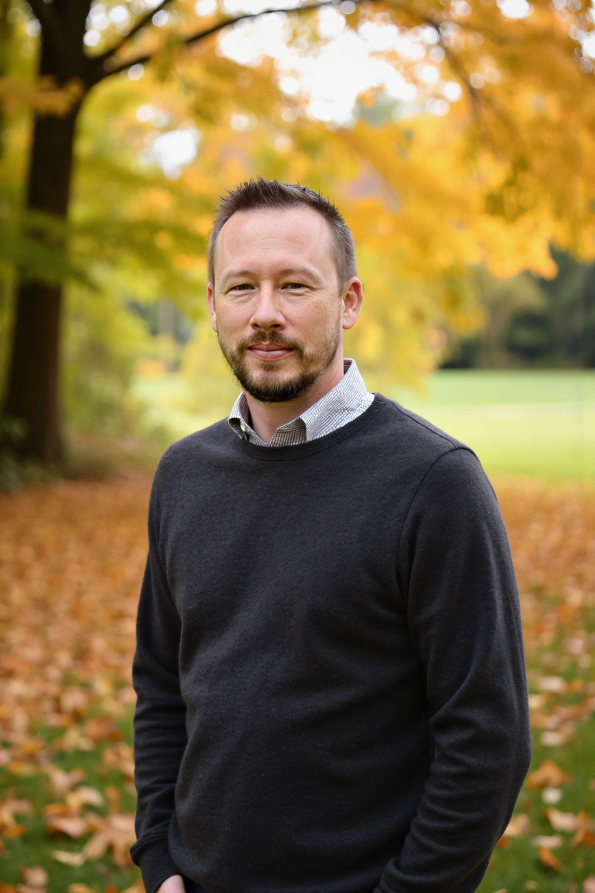 Man standing in a park surrounded by autumn leaves and trees.