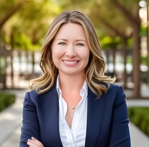 A smiling woman in a navy blazer stands outdoors with trees in the background.