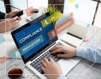 Person typing on a laptop with keywords related to compliance and regulations visible