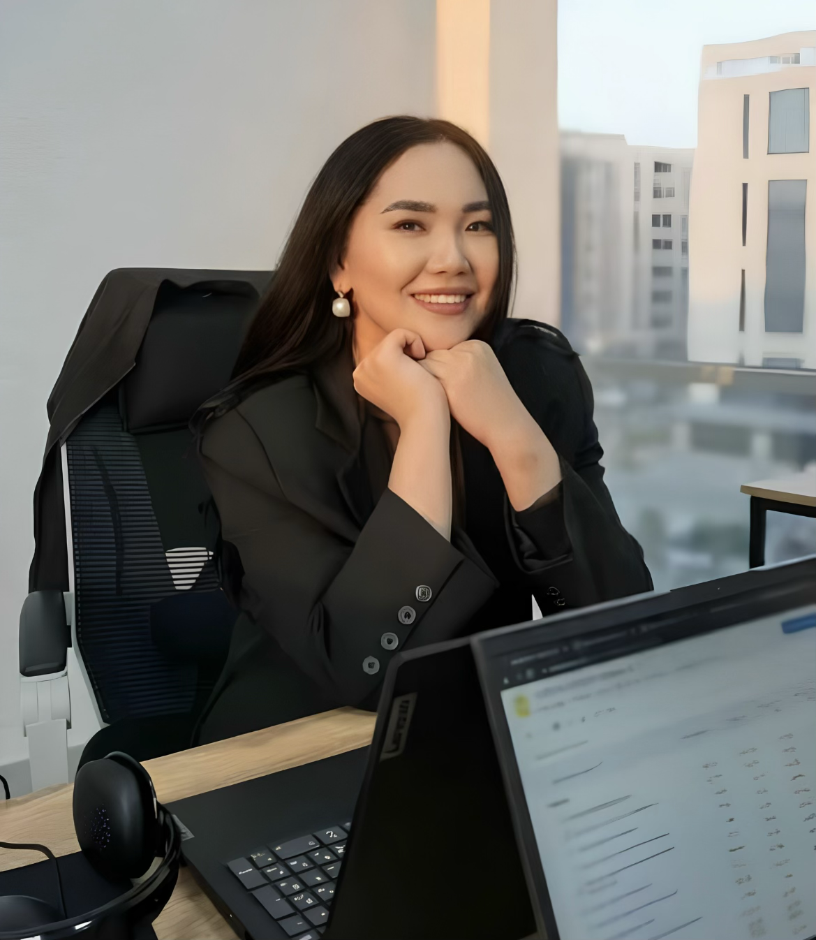 Woman in a business suit smiling at her desk with a laptop and headset