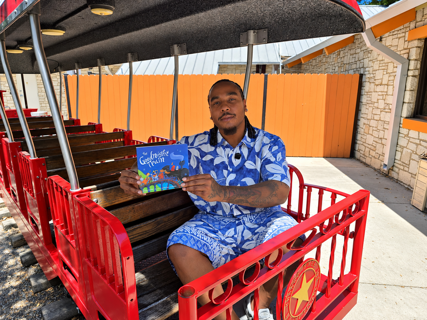 A person in a blue floral outfit sits on a red train car holding a book