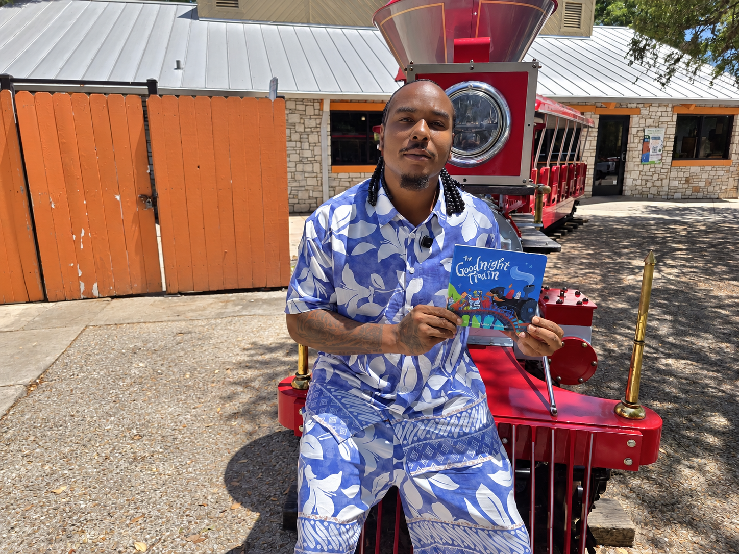 Person holding a children's book while sitting on a red train in a park