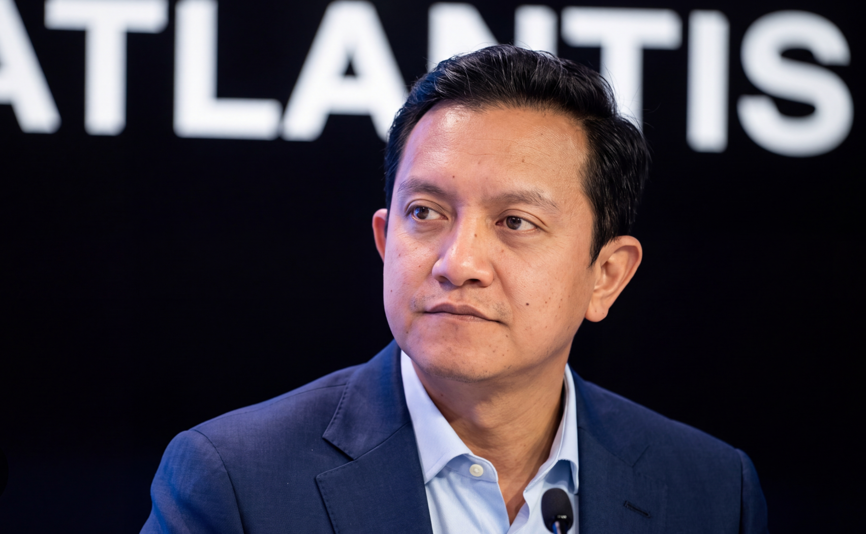 A man in a suit listens attentively during a press conference setting