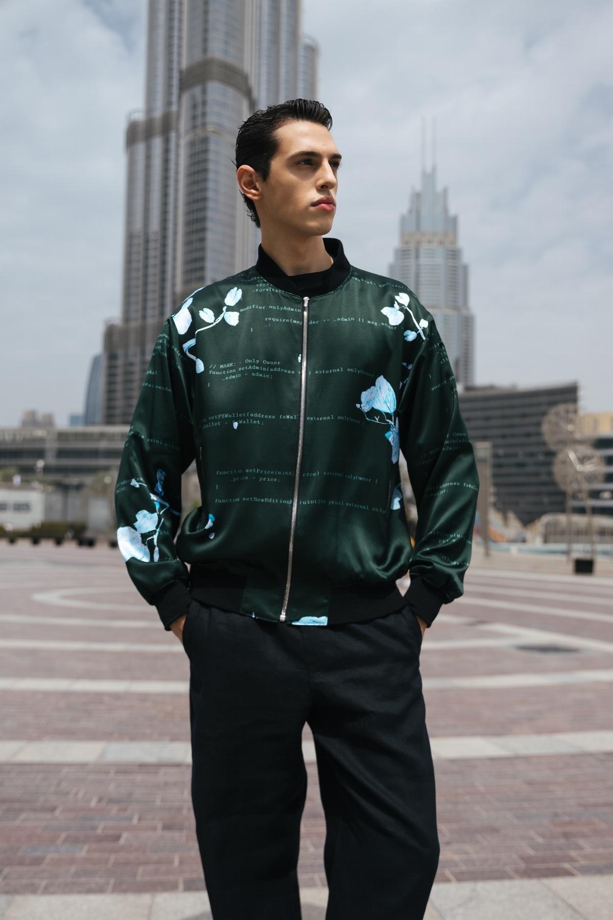 Man in a floral bomber jacket poses in an urban setting with skyscrapers.