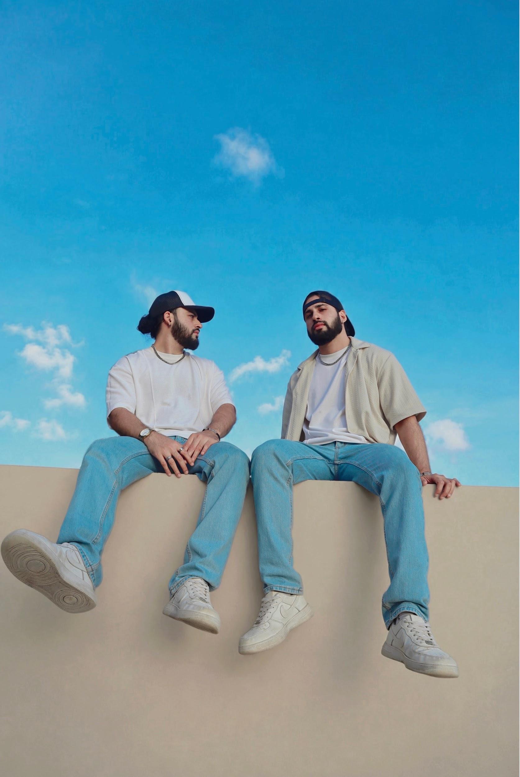 Two men sitting on a ledge against a blue sky with clouds