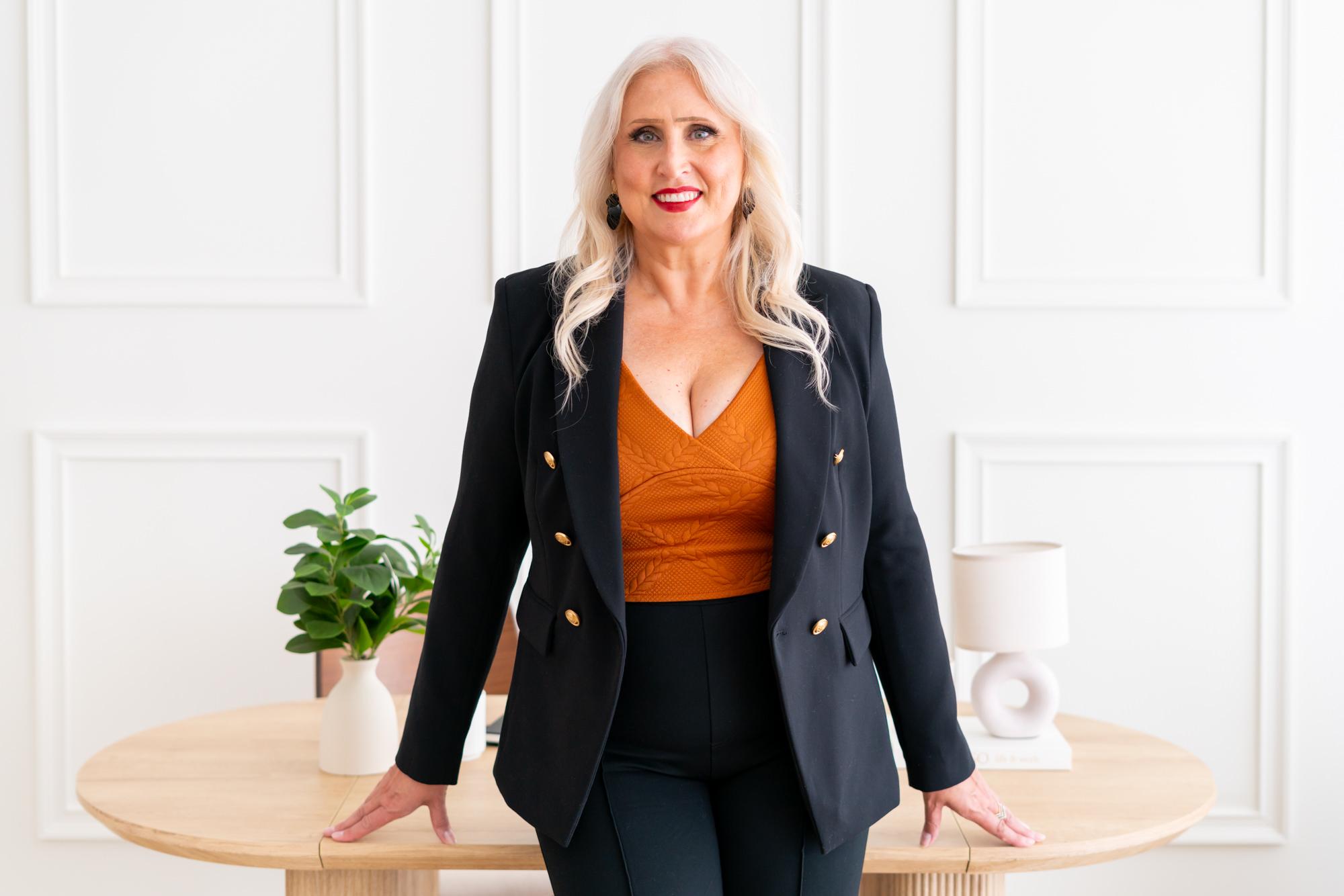 Woman in a stylish outfit stands confidently by a table with decor.