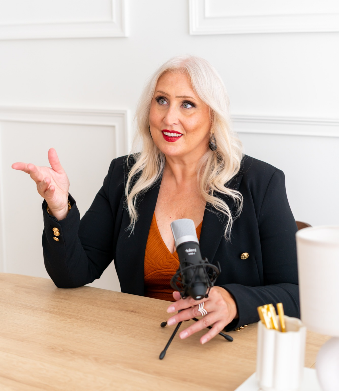 A woman with blonde hair speaks animatedly at a table with a microphone