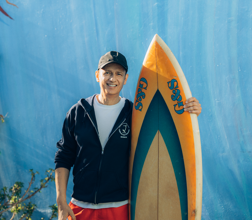 Man smiling while holding a surfboard against a blue backdrop