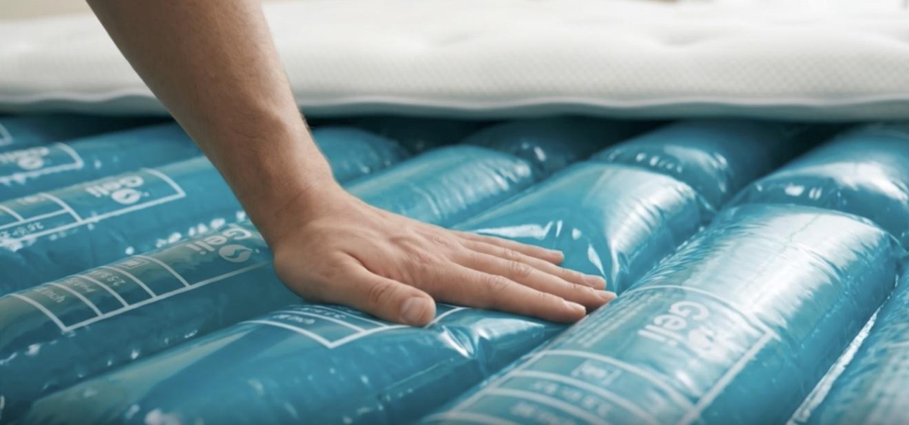 Hand pressing down on blue gel mattress layers with a white mattress top