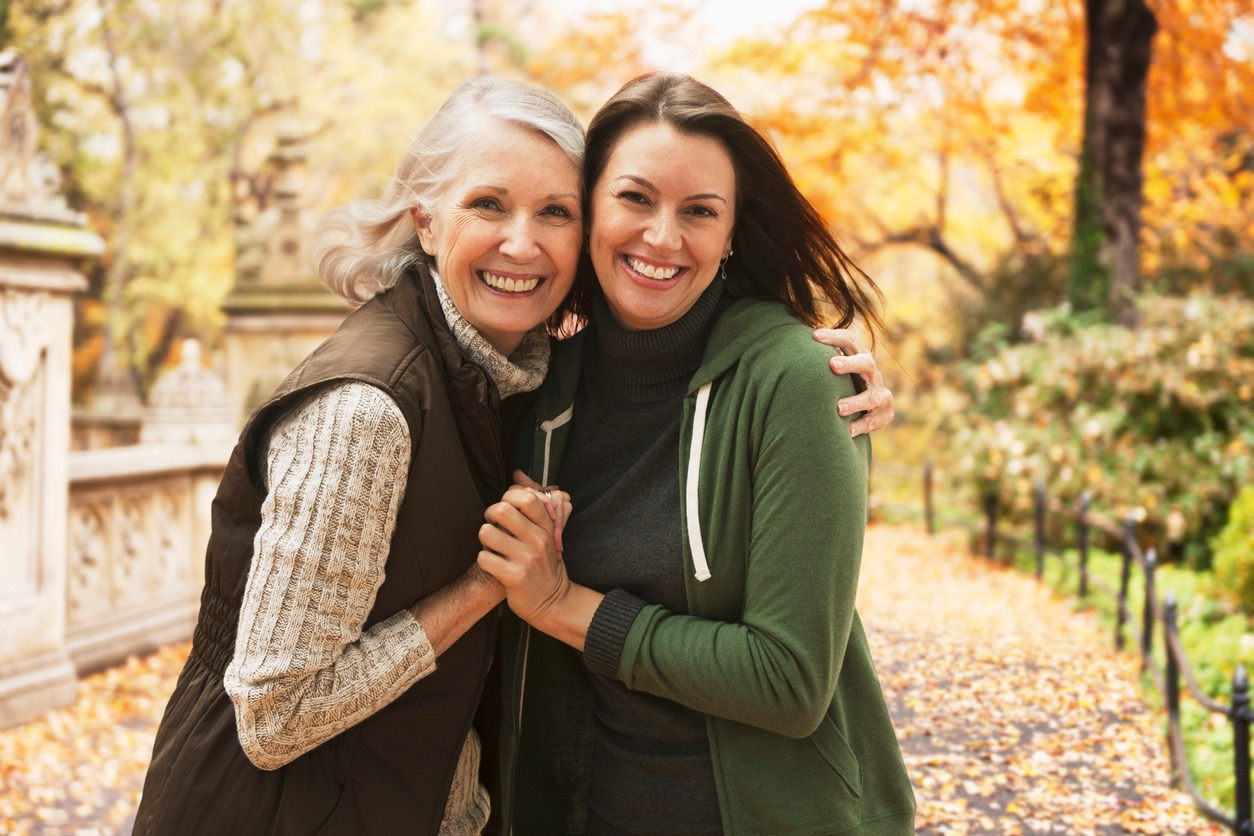 Two women smiling and embracing in a picturesque autumn park setting