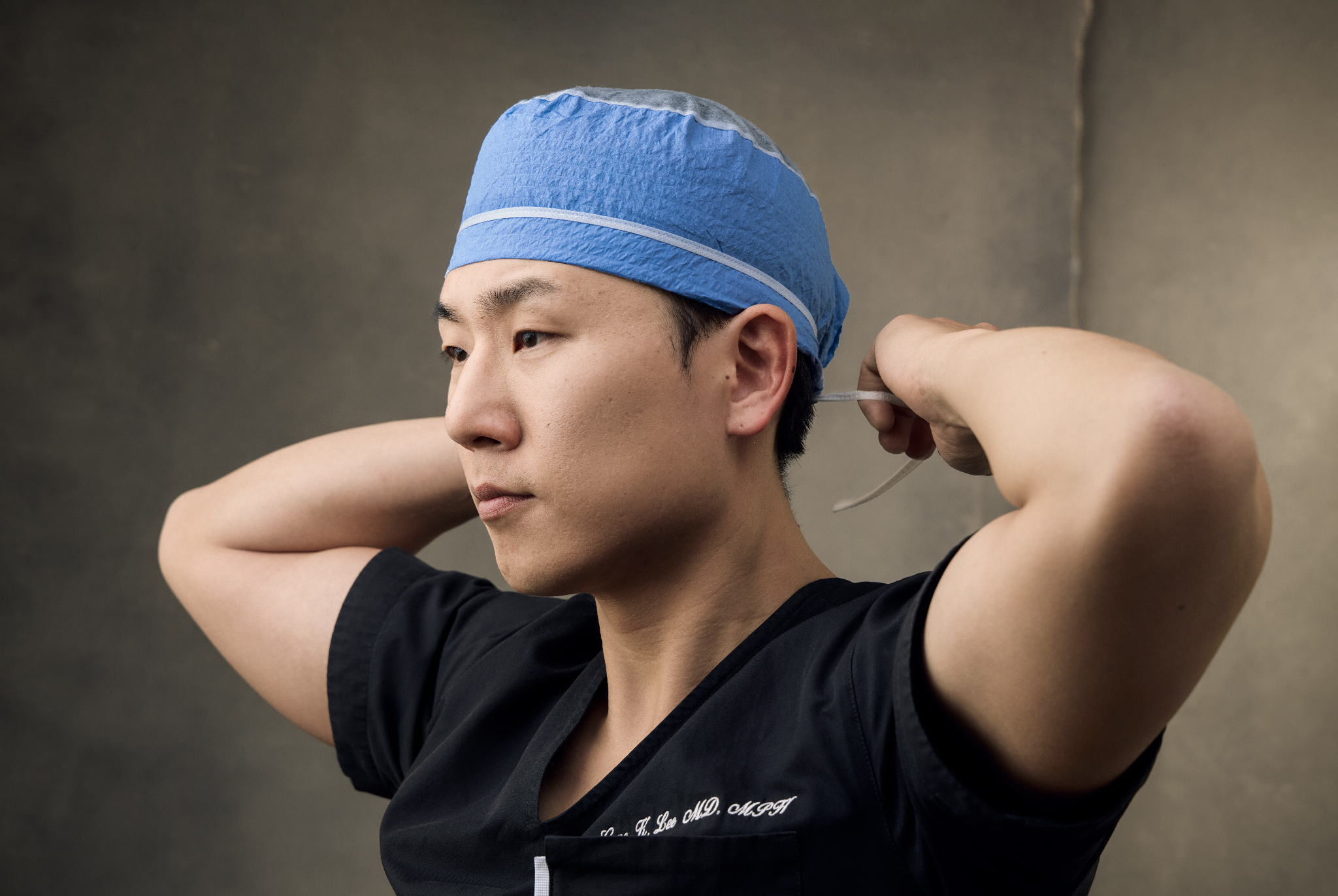 A male surgeon in a surgical cap prepares for surgery, showing focused determination