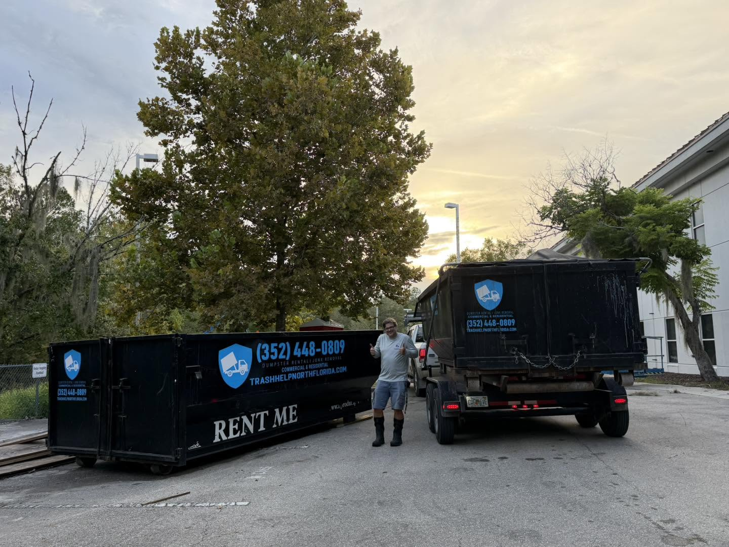 Two dumpsters next to a truck with a man standing beside them at sunset