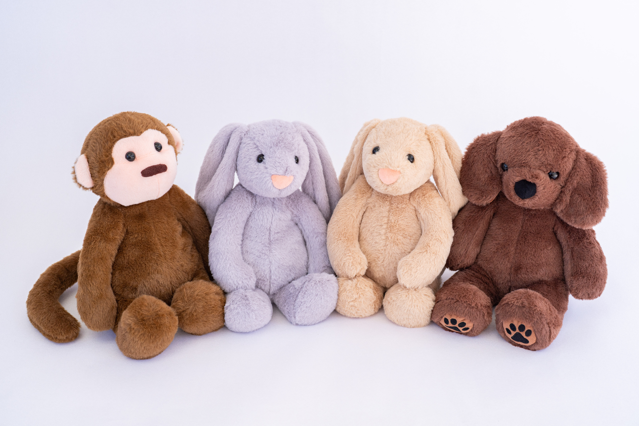 Four soft plush toys: a monkey, two bunnies, and a dog sitting side by side