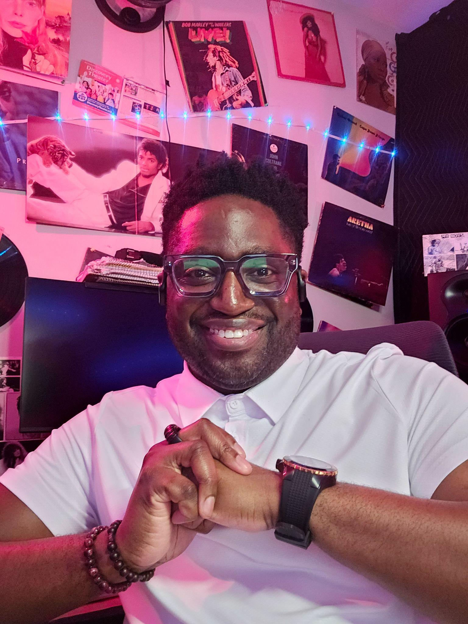 Smiling man in a white polo shirt poses in a decorated studio with posters