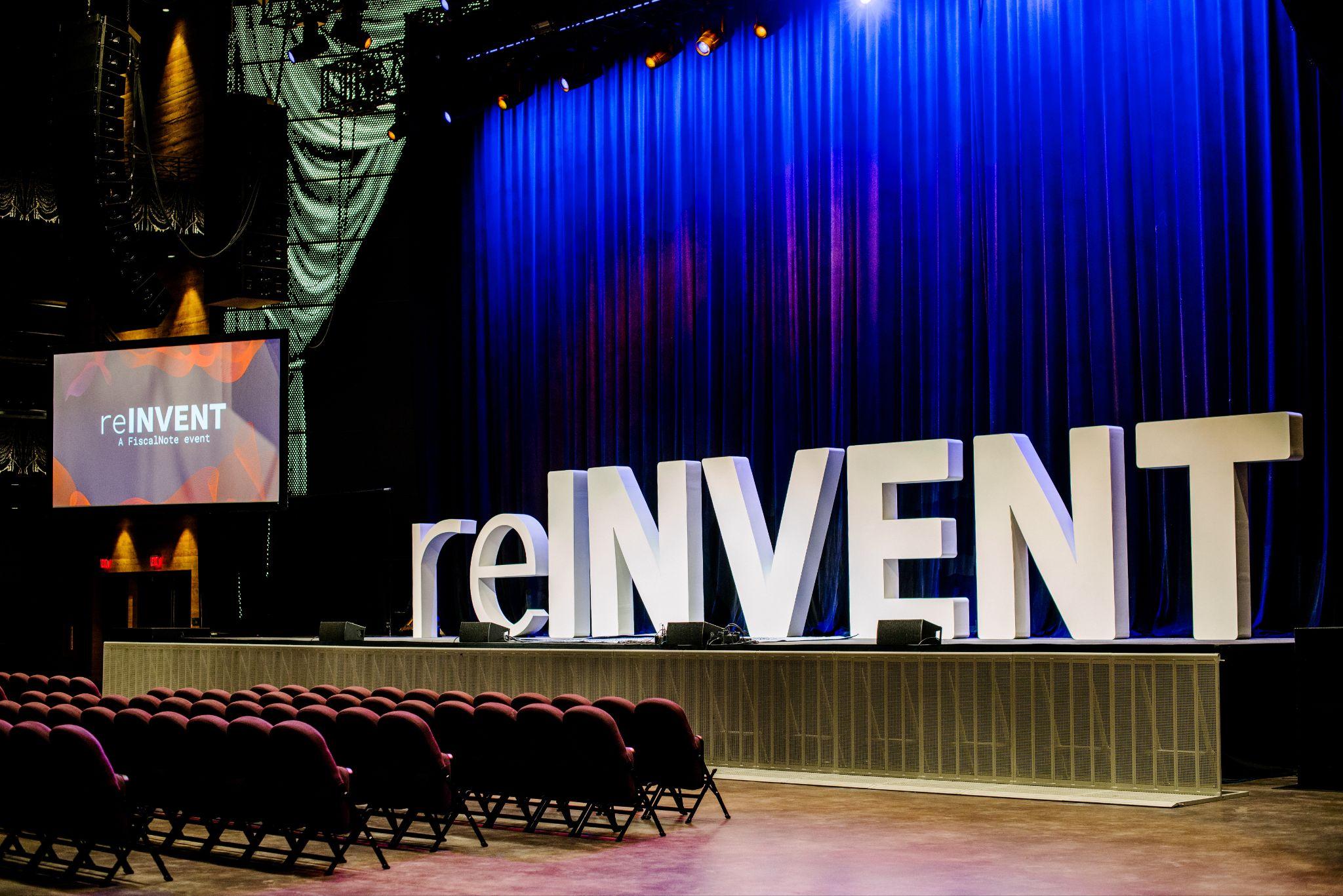 Stage setup for reINVENT event with large letters and a blue curtain backdrop