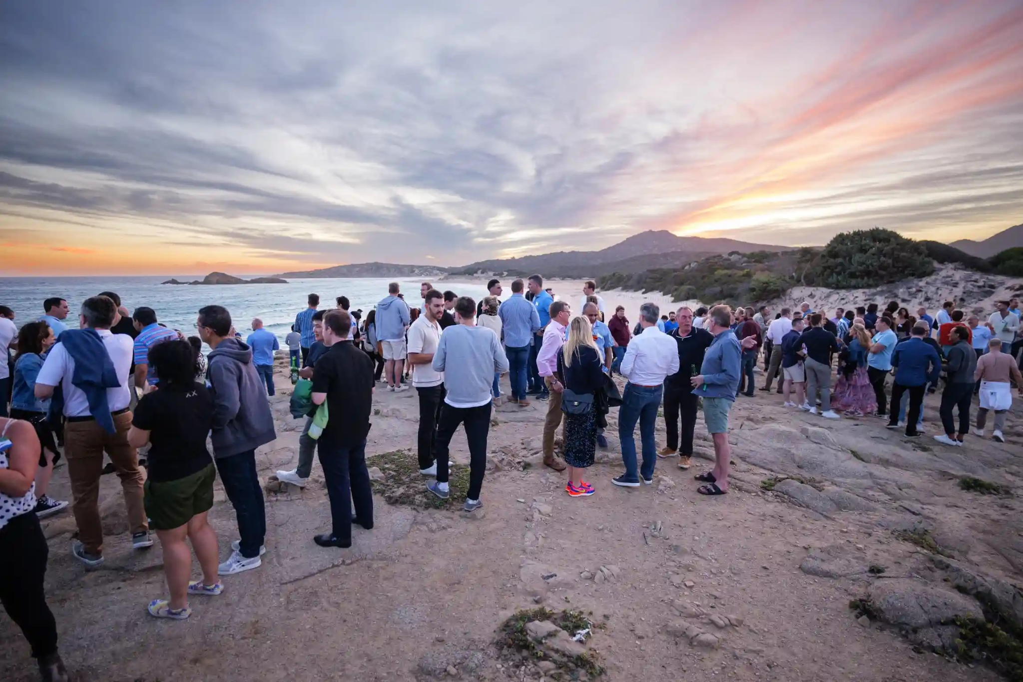 Group of people gathered by the seaside during sunset on rocky terrain