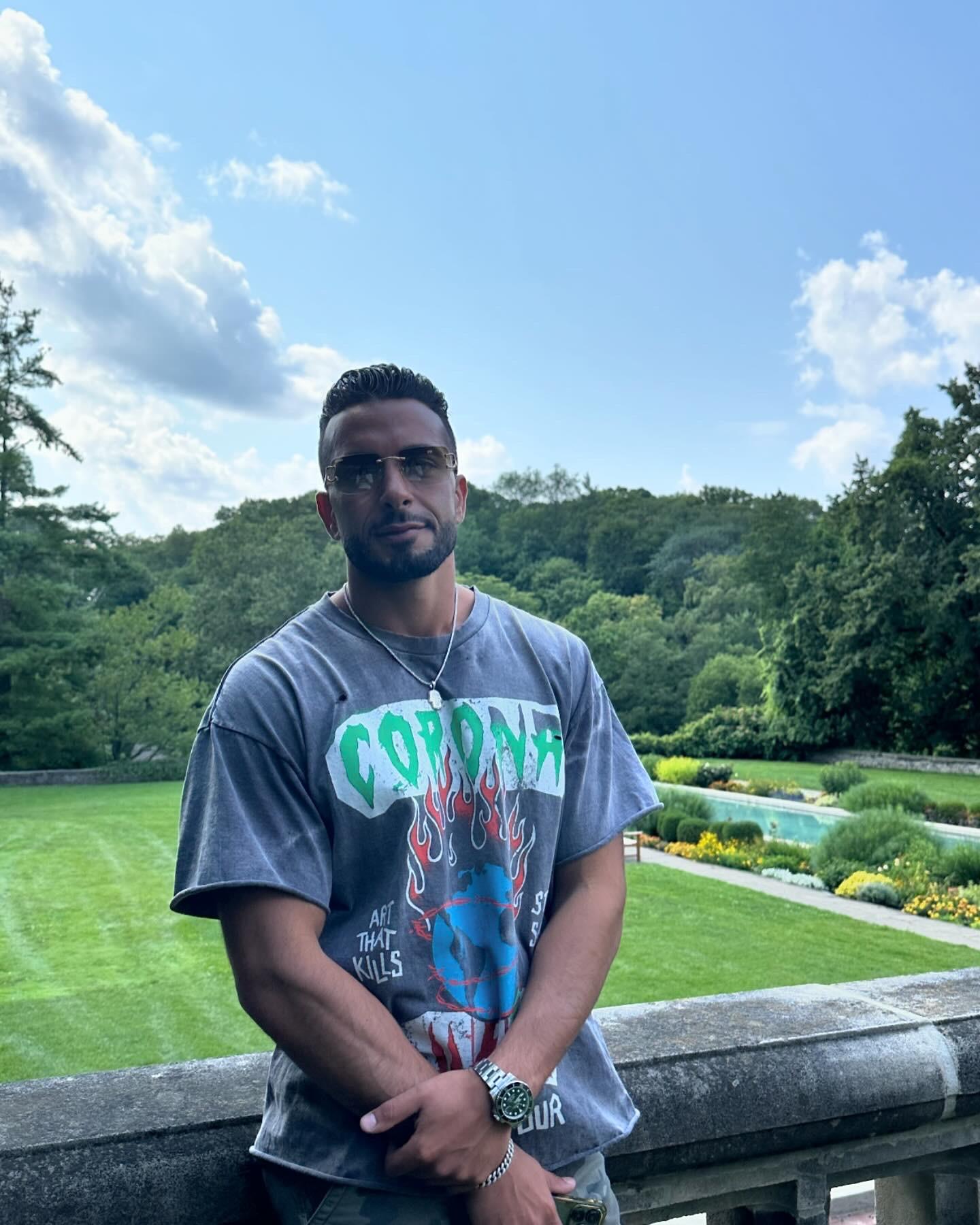 Man stands outdoors in casual clothing with a lush landscape in the background