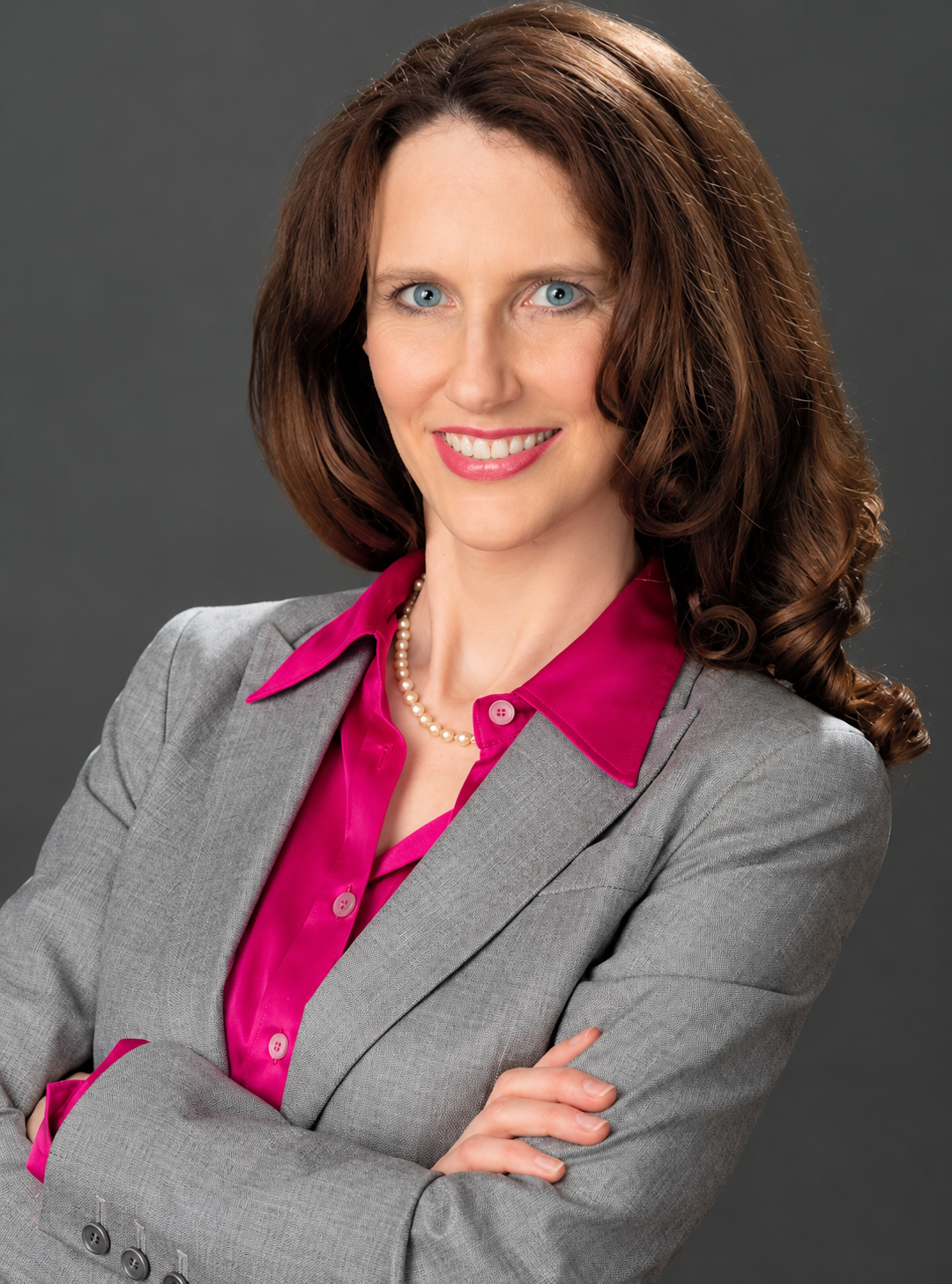Professional woman in a gray suit with a pink blouse, smiling confidently