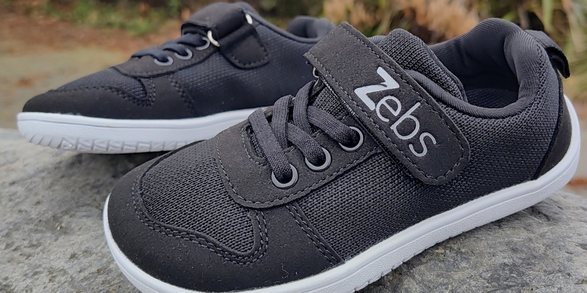 Black sneakers with a Velcro strap and laces placed on a rock surface