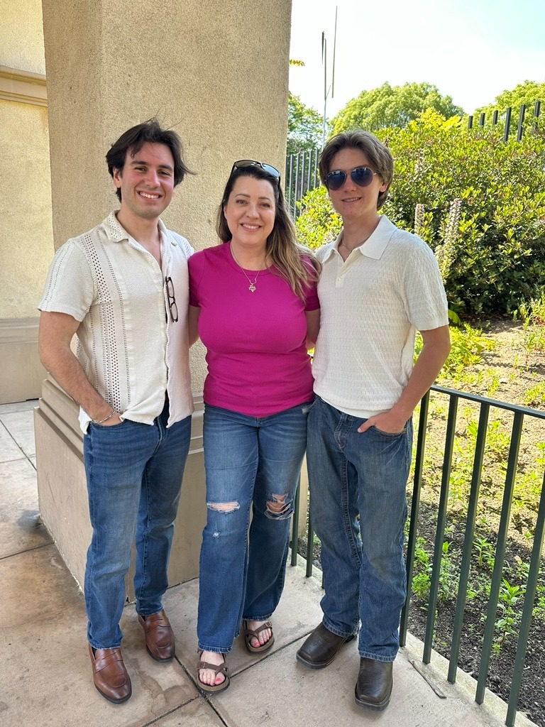 Three people pose together outdoors, smiling, in casual summer attire.
