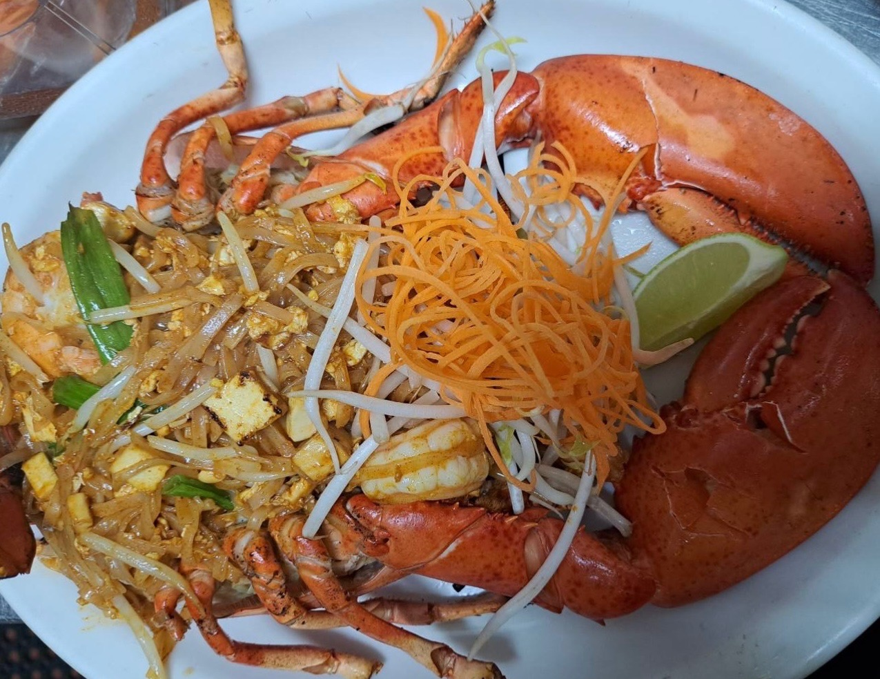 Plated seafood dish with lobster, shrimp, and stir-fried noodles garnished with vegetables