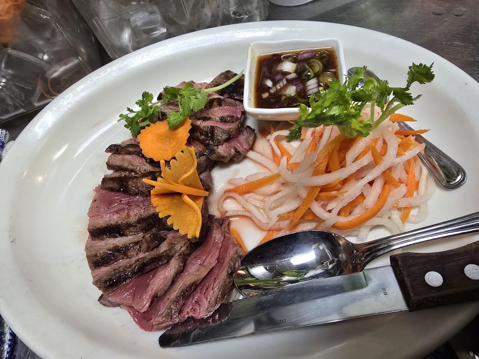 Plated grilled steak with herbs, carrot garnish, and a side of pickled vegetables