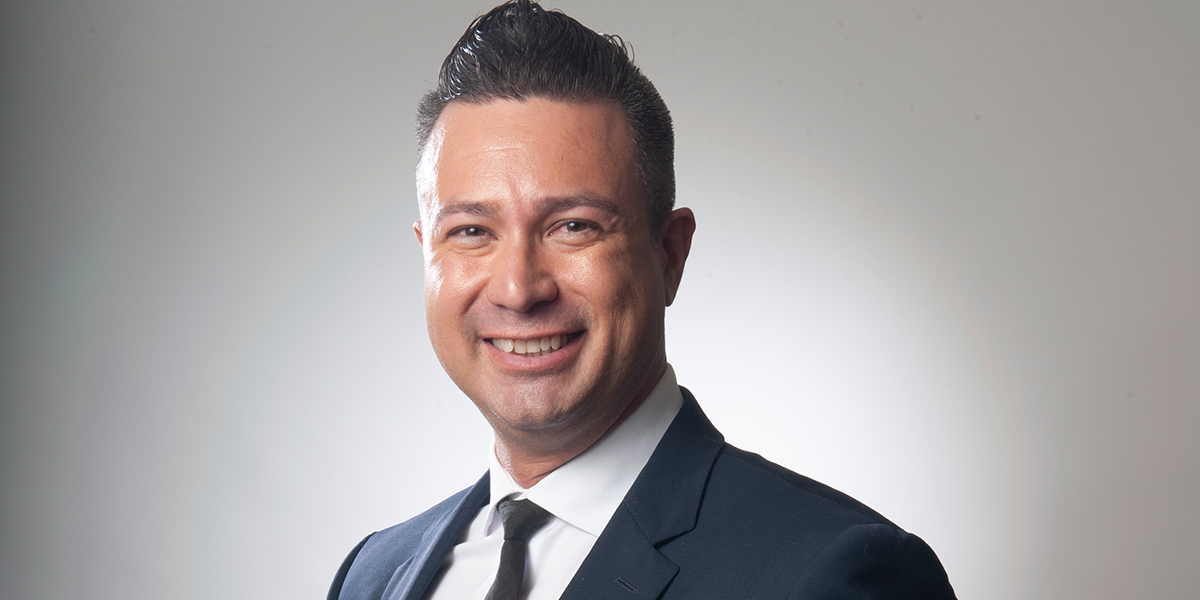 Smiling man in a dark suit and tie against a light background