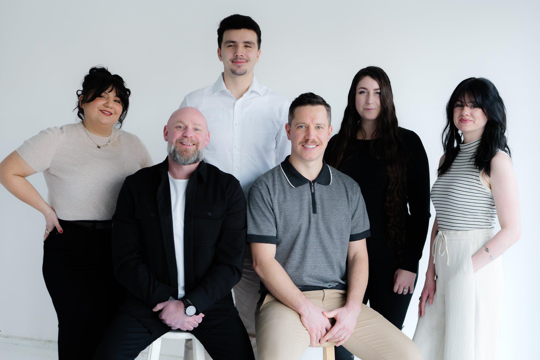 Group portrait of six individuals smiling against a plain white background