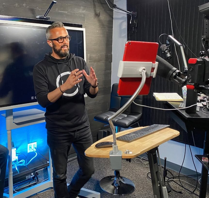 Man gesturing while presenting in a studio setup with cameras and screens