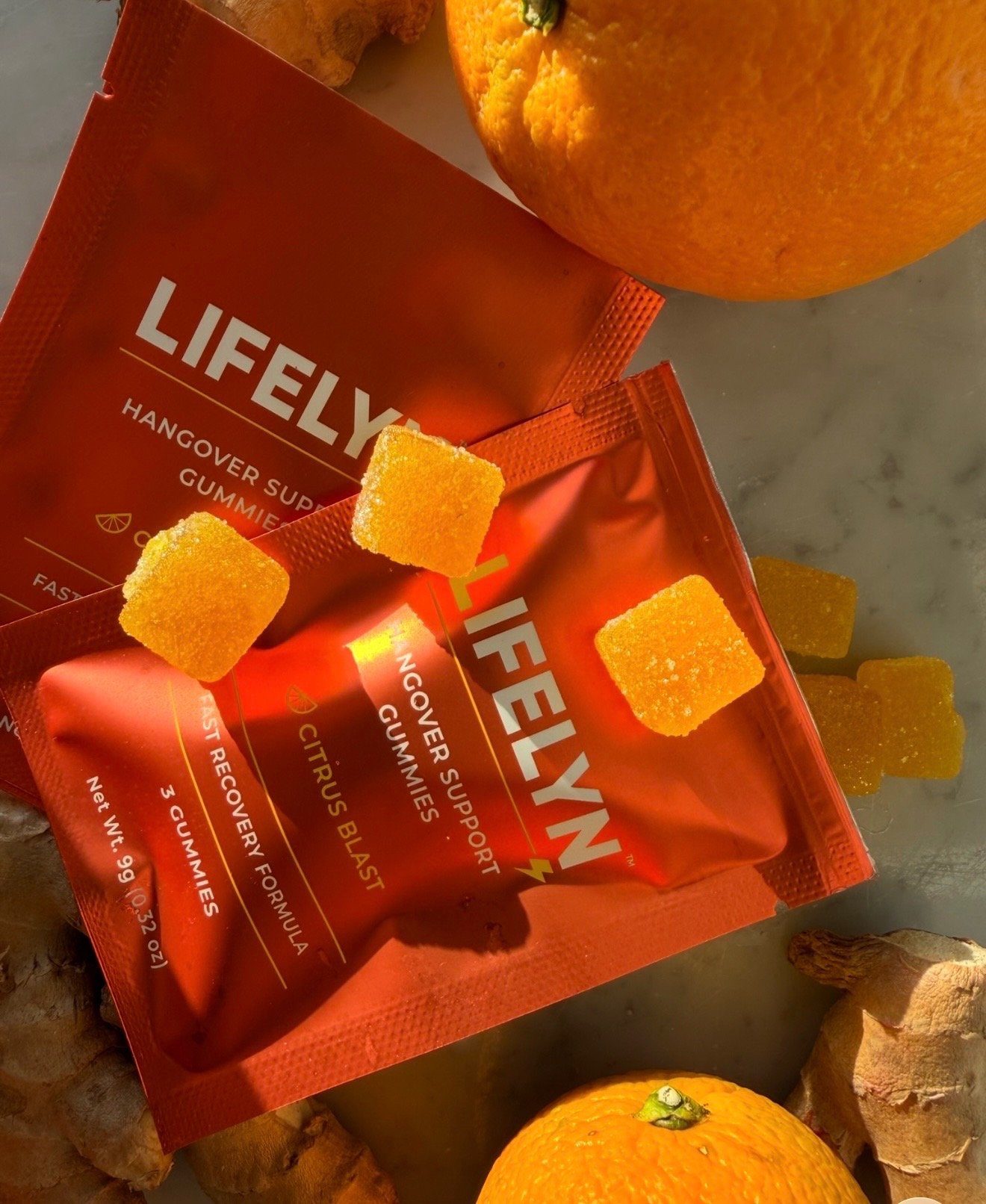 Two packages of Lifelym hangover support gummies beside oranges and ginger root pieces