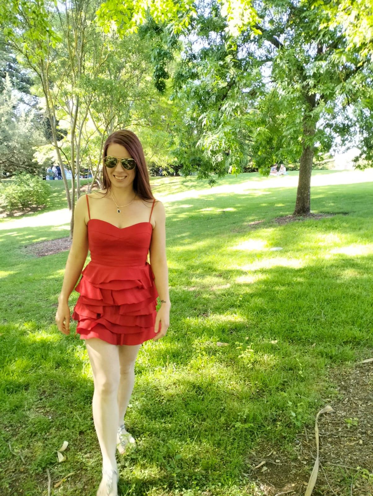 A woman in a red dress walks through a sunny, green park setting