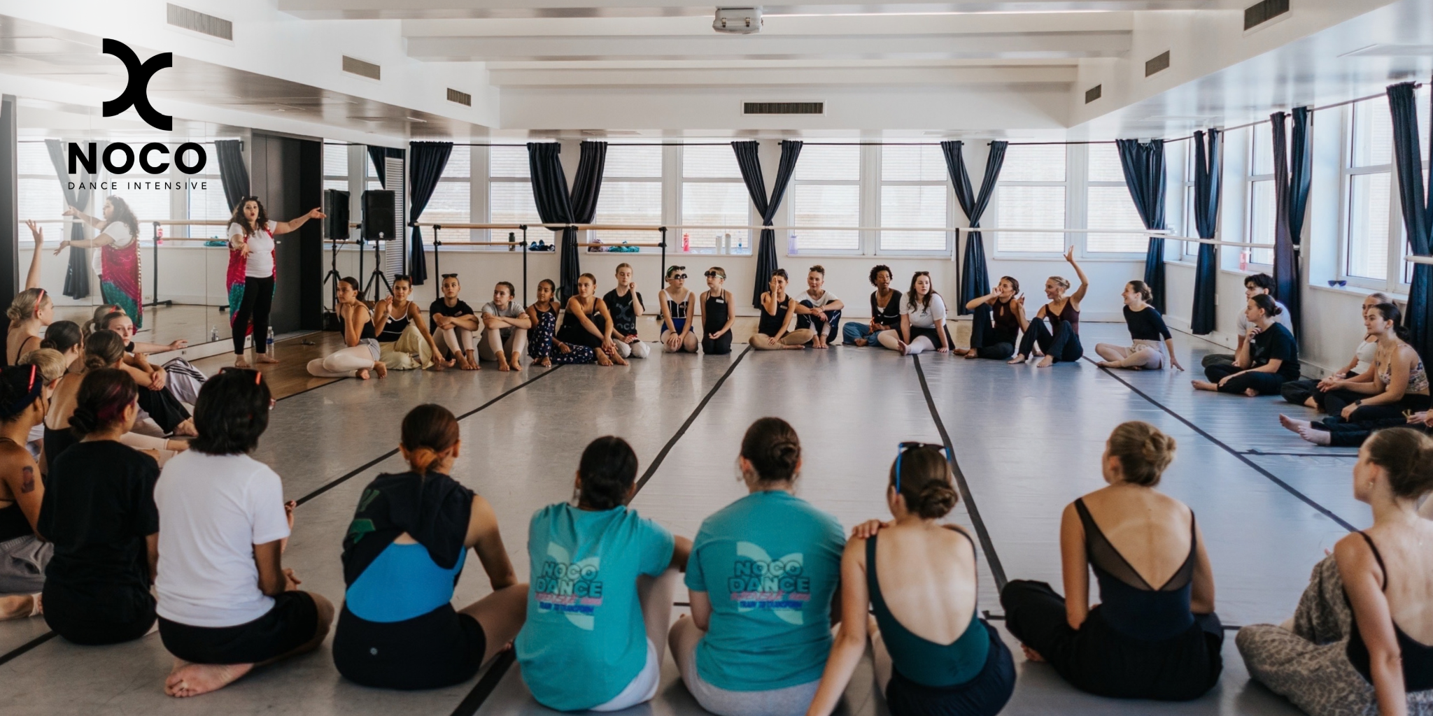 A dance workshop with participants seated in a studio, engaging in discussion and learning.