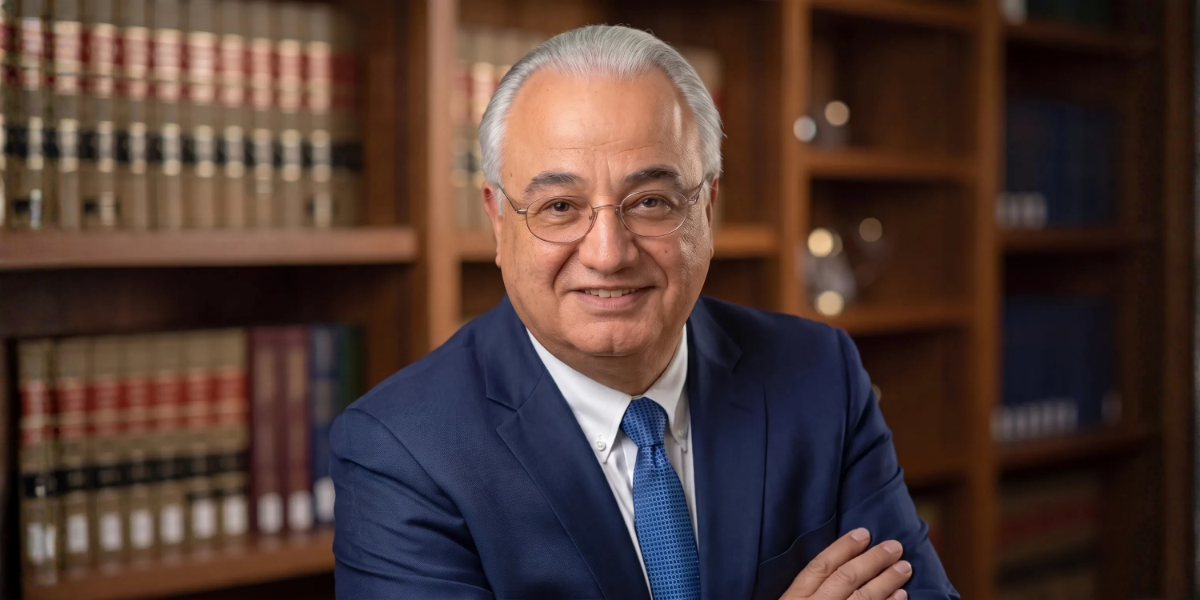 Smiling middle-aged man in a suit, standing in a library with bookshelves behind him