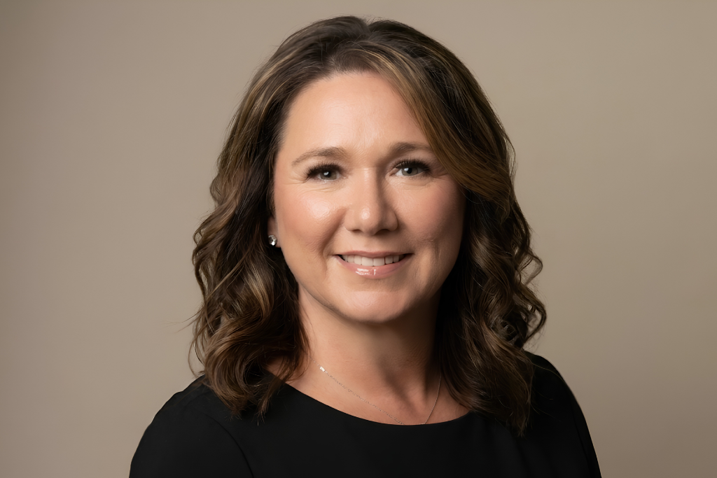 Smiling woman with wavy brown hair wearing a black shirt, neutral background