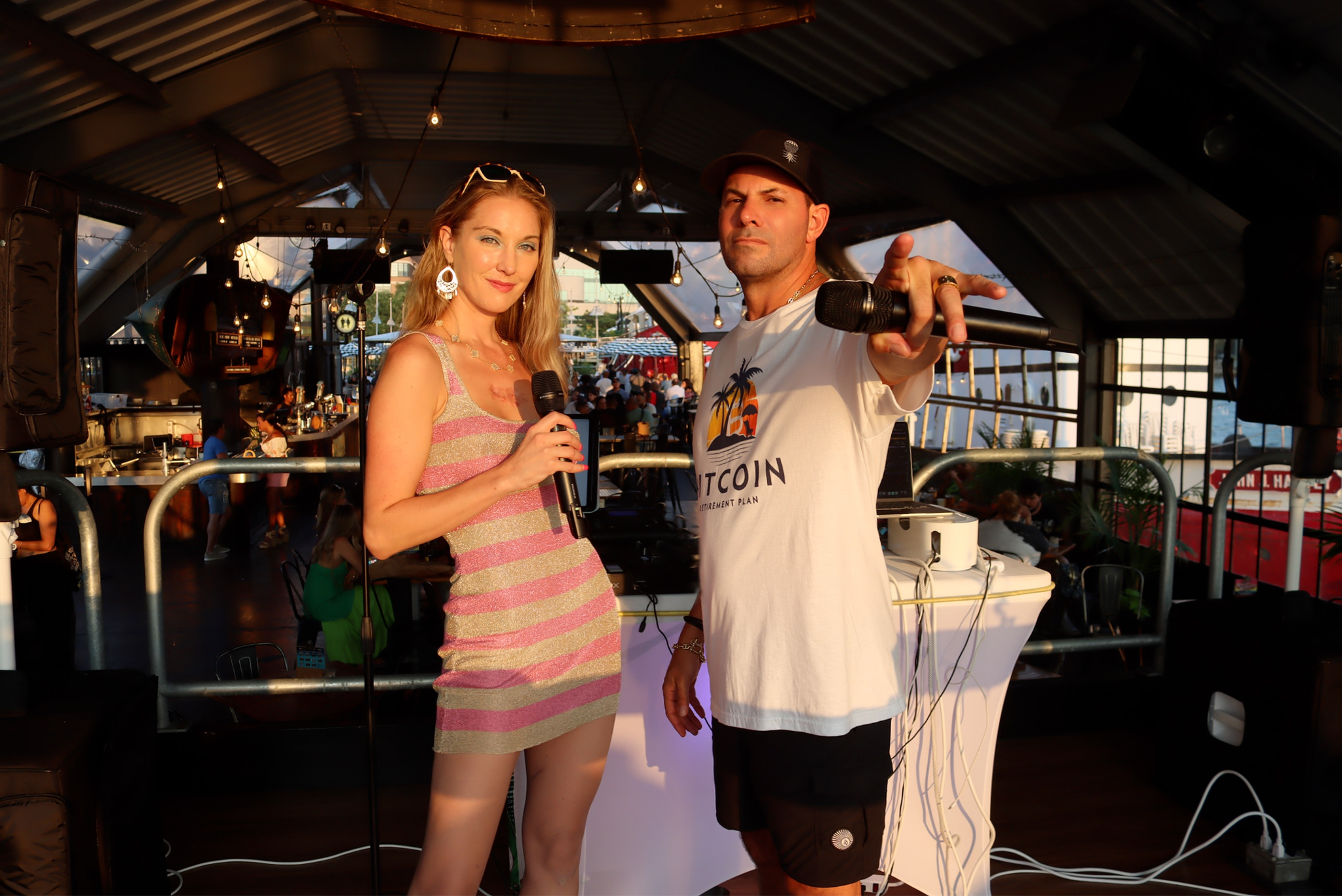 Two people holding microphones stand on stage in a lively venue.