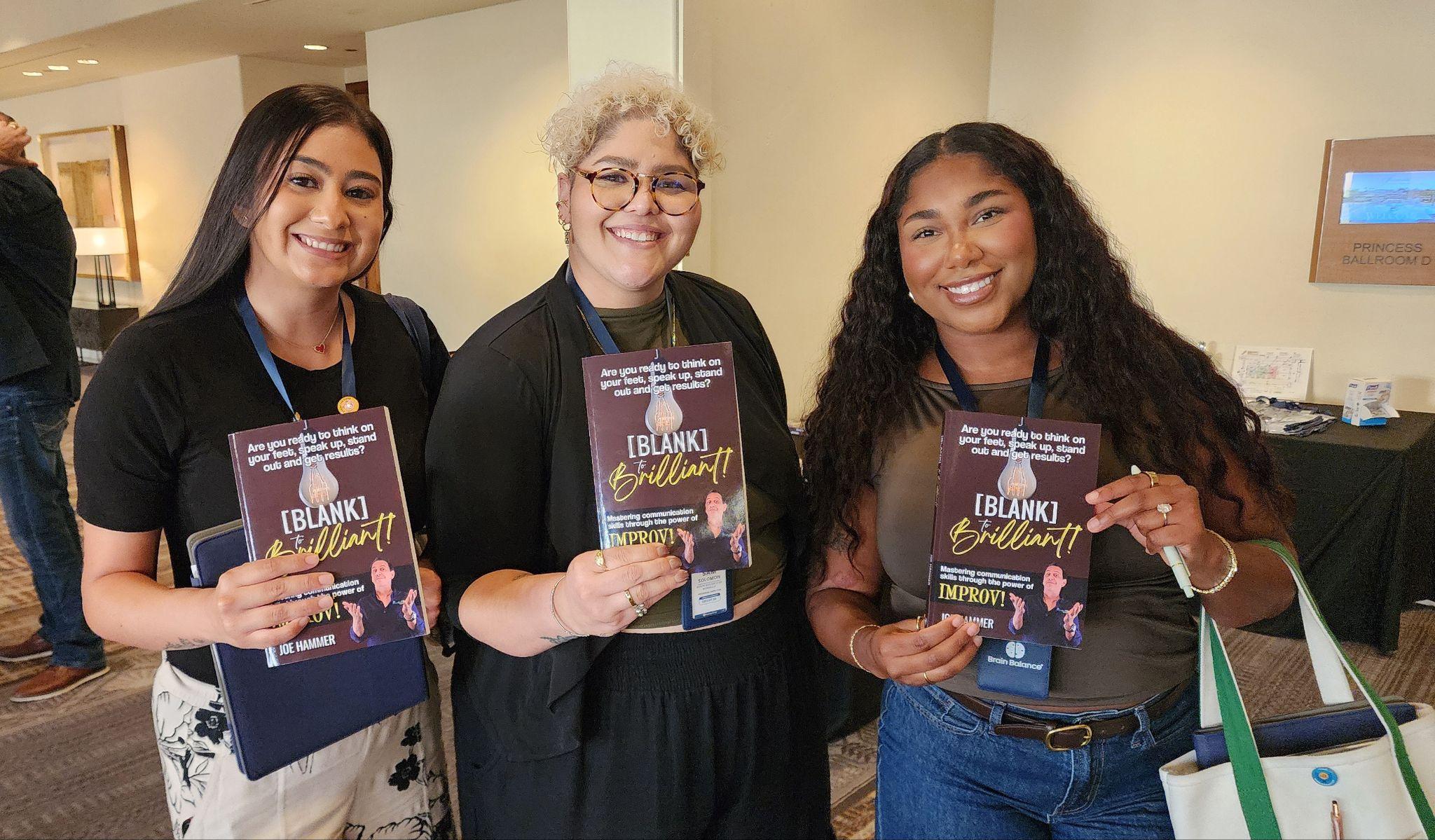 Three women holding books and smiling at a conference event