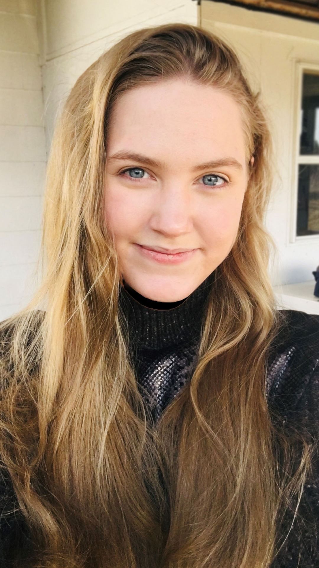 Young woman with long blonde hair smiling in a cozy outdoor setting