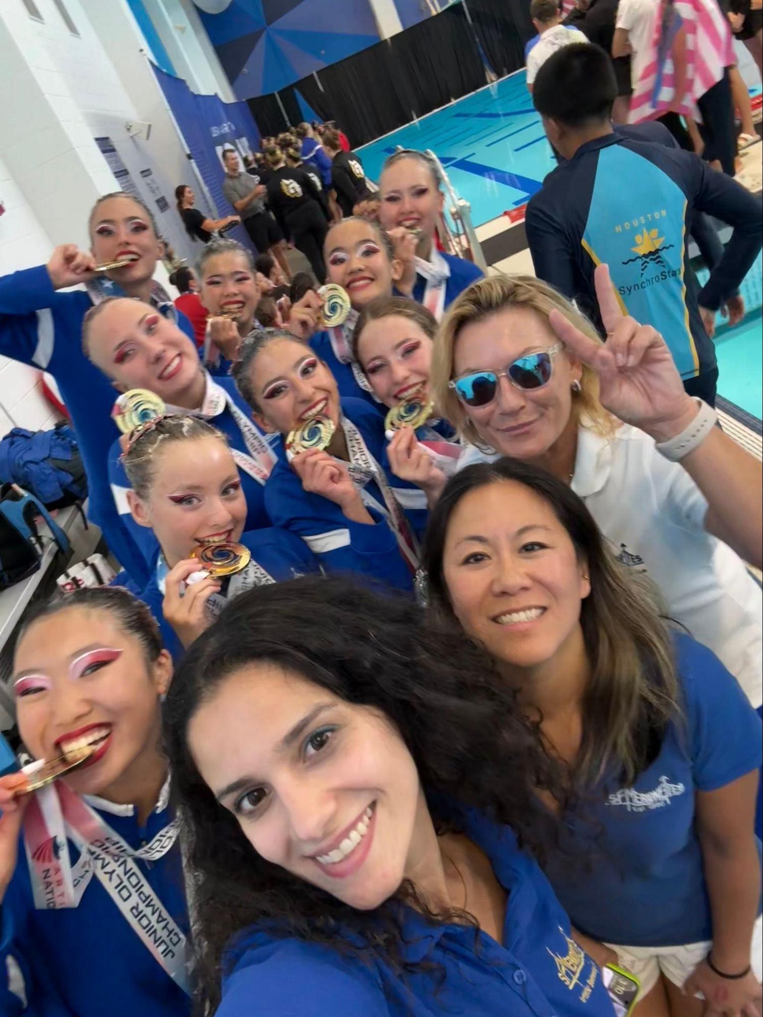 A group celebrating with medals at a synchronized swimming event with a pool in background