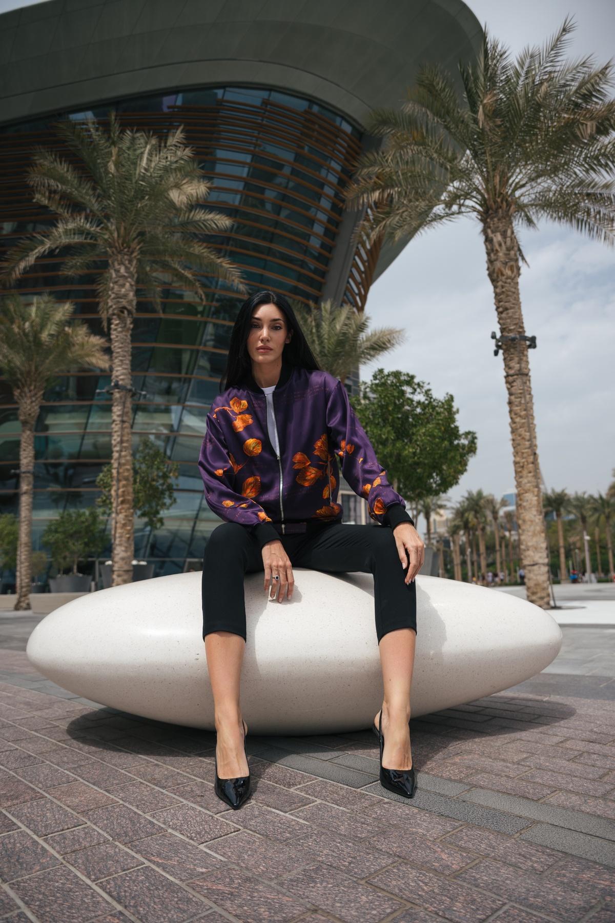 A woman in a colorful jacket sits on a large white sculpture outdoors.
