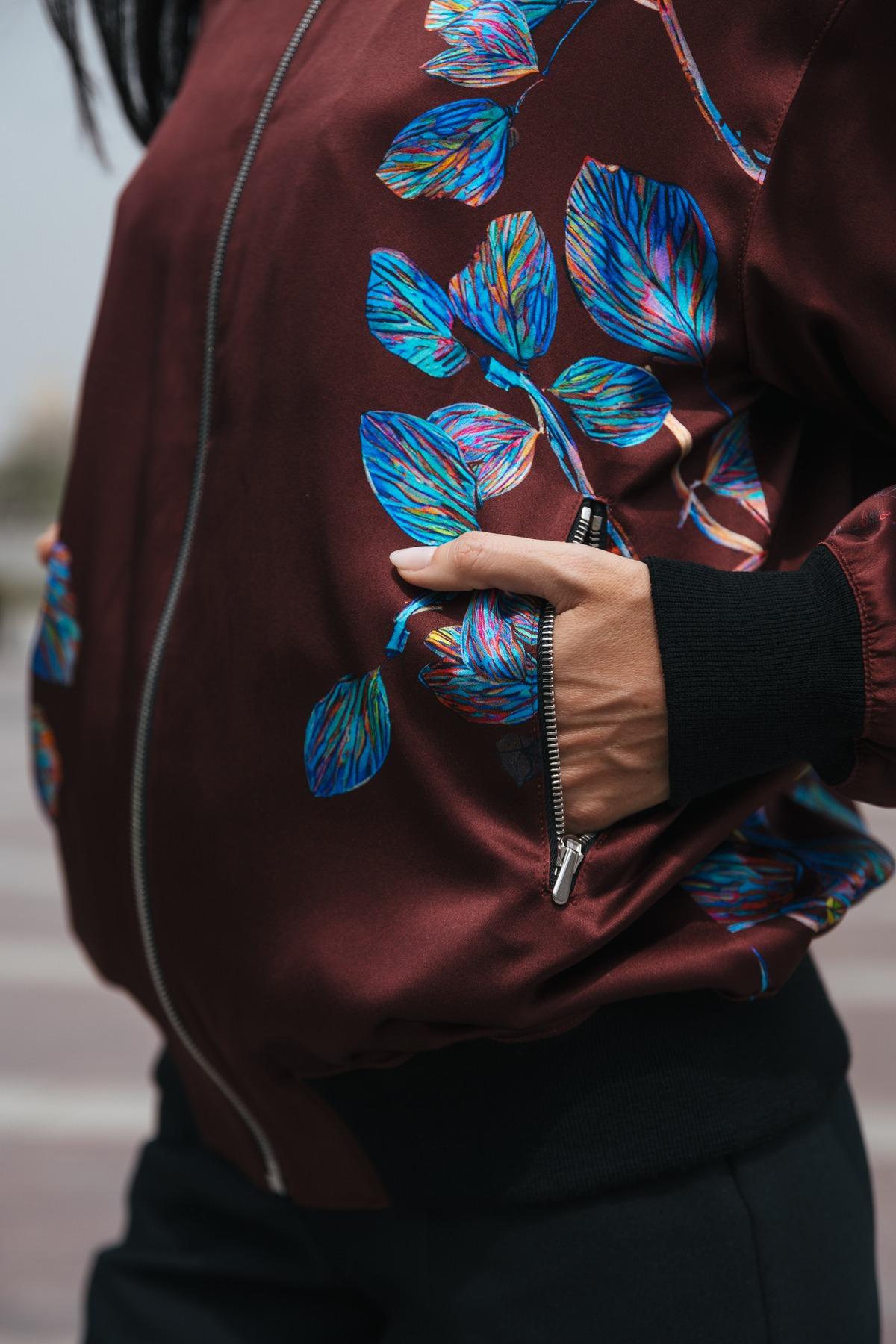 Close-up of a person wearing a floral bomber jacket with a pocket.