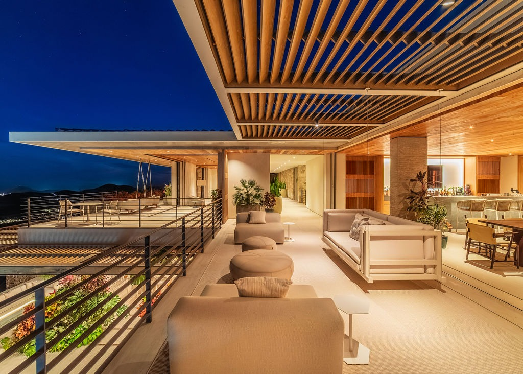 Modern outdoor lounge area with comfortable seating under a slatted roof at night.