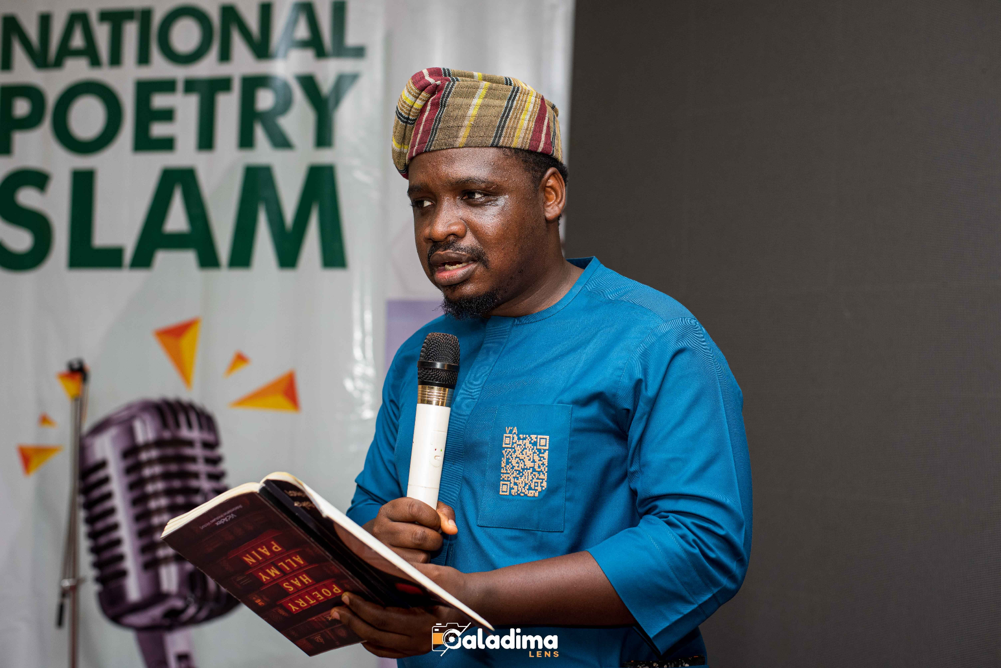 Man in traditional attire reads from a book at a poetry slam event