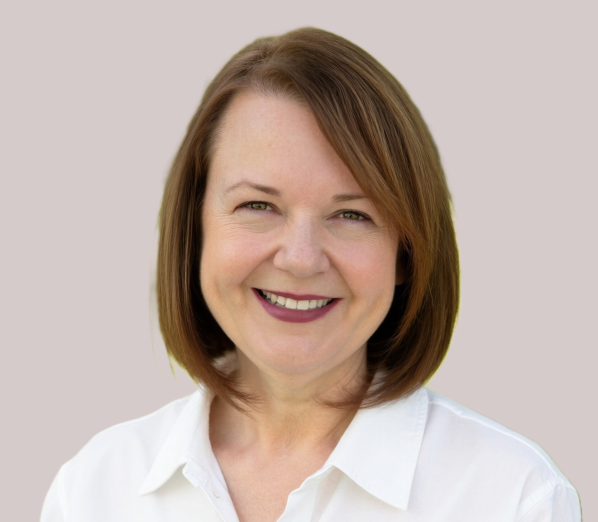 Smiling woman with shoulder-length brown hair wearing a white blouse against a neutral background