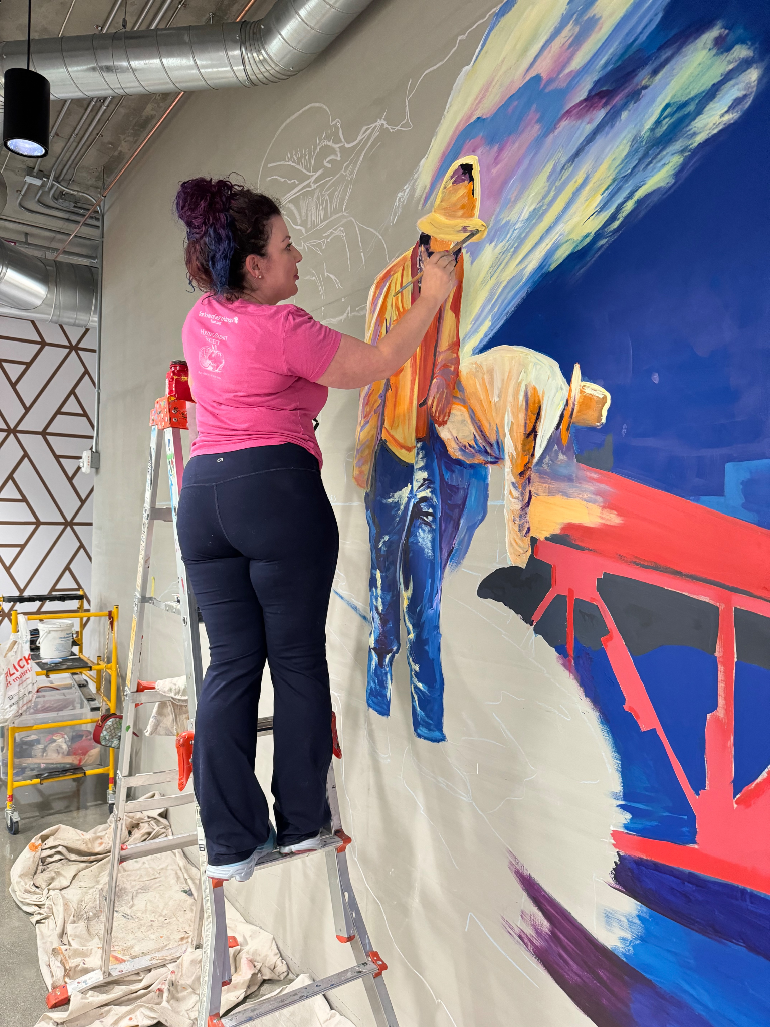 Artist painting a colorful mural while standing on a ladder indoors