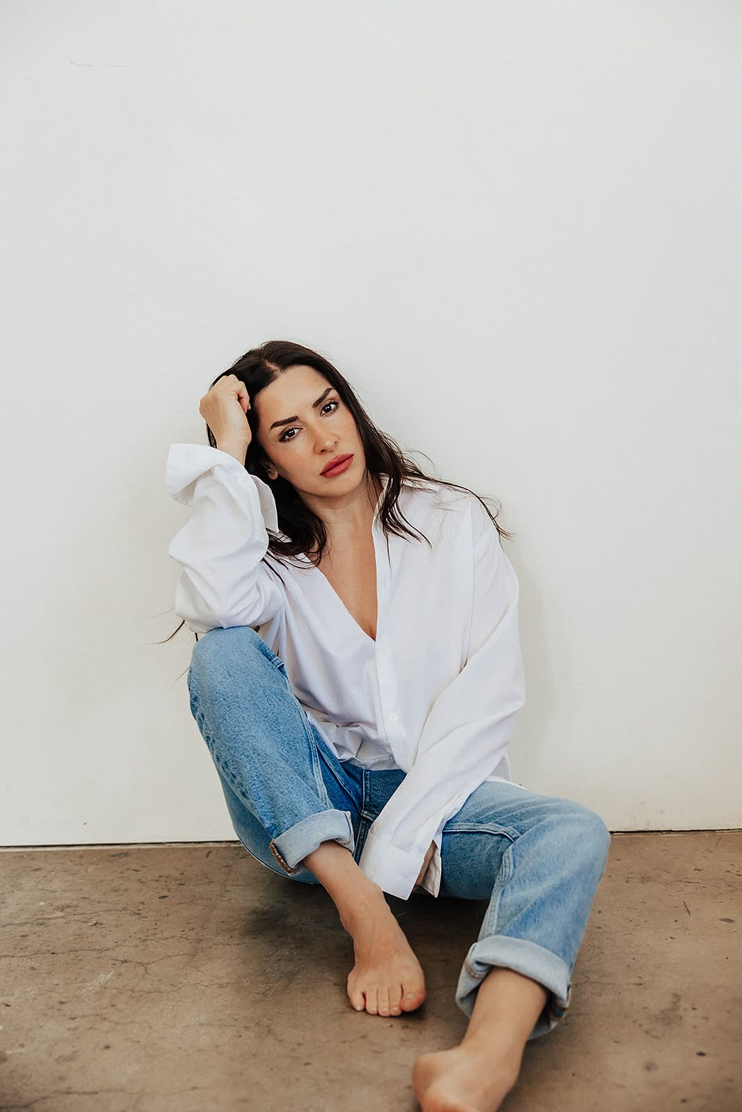 A woman seated on the floor wearing a white button-up shirt and jeans