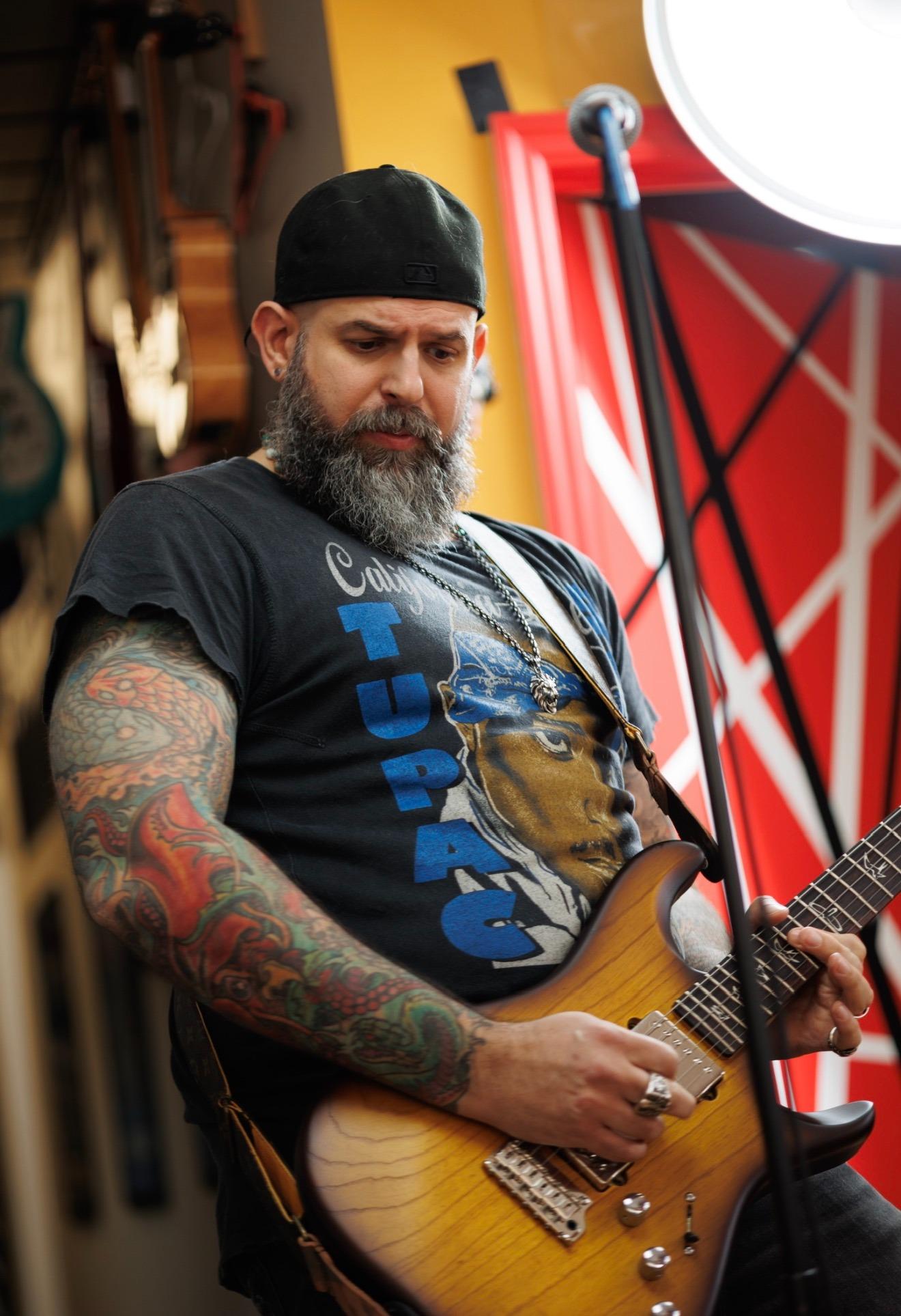 Man with tattoos playing guitar, wearing a cap and a graphic t-shirt