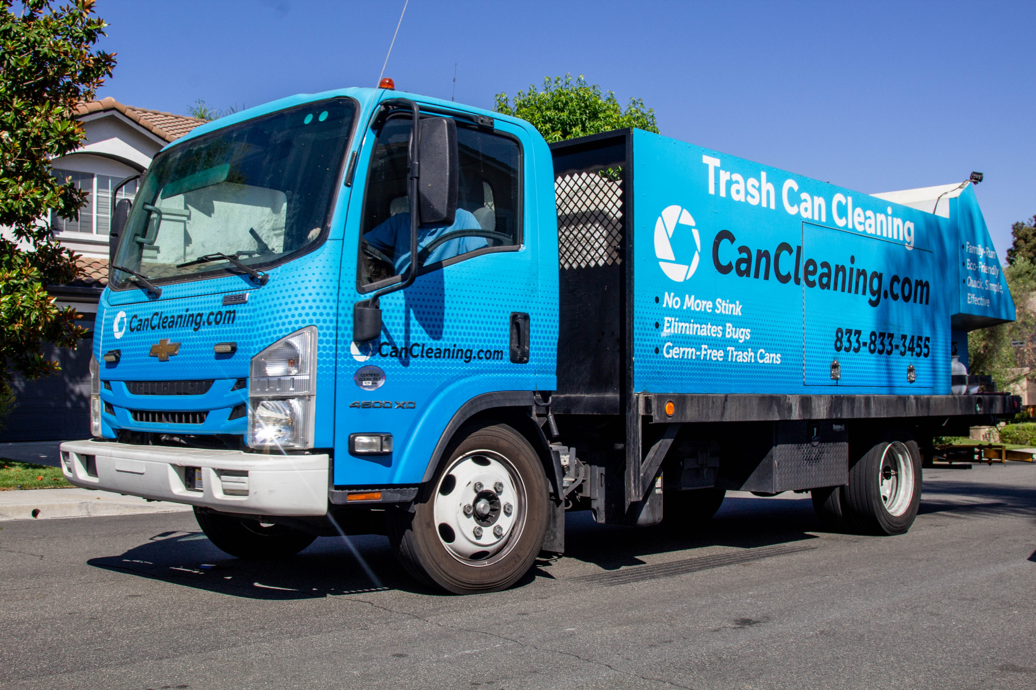 A blue garbage truck promoting a trash can cleaning service parked on a street